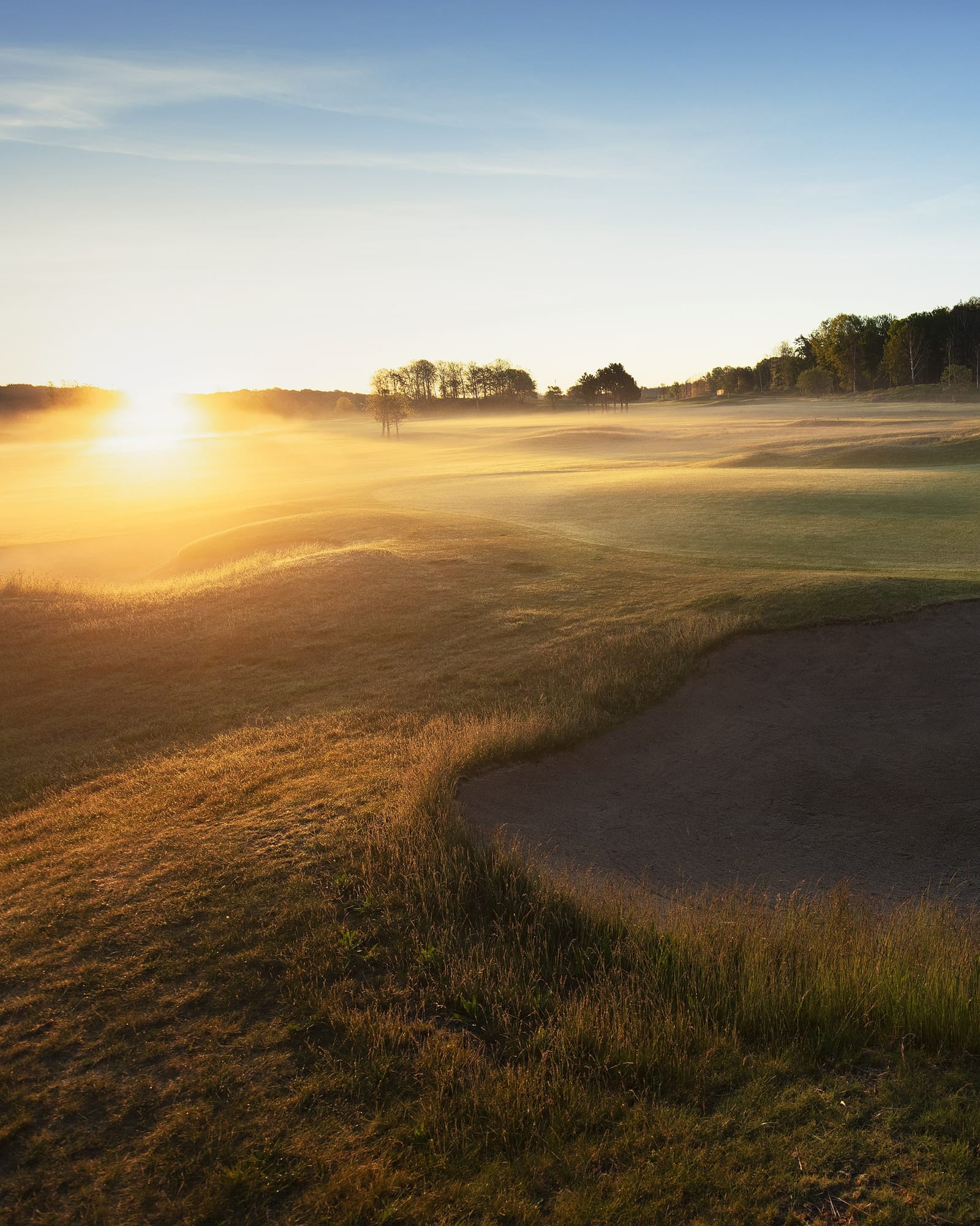 Golf course at sunrise with mist over the fairway and a bunker in the foreground